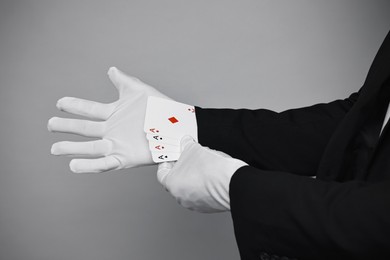 Photo of Illusionist taking playing cards out of sleeve on grey background, closeup