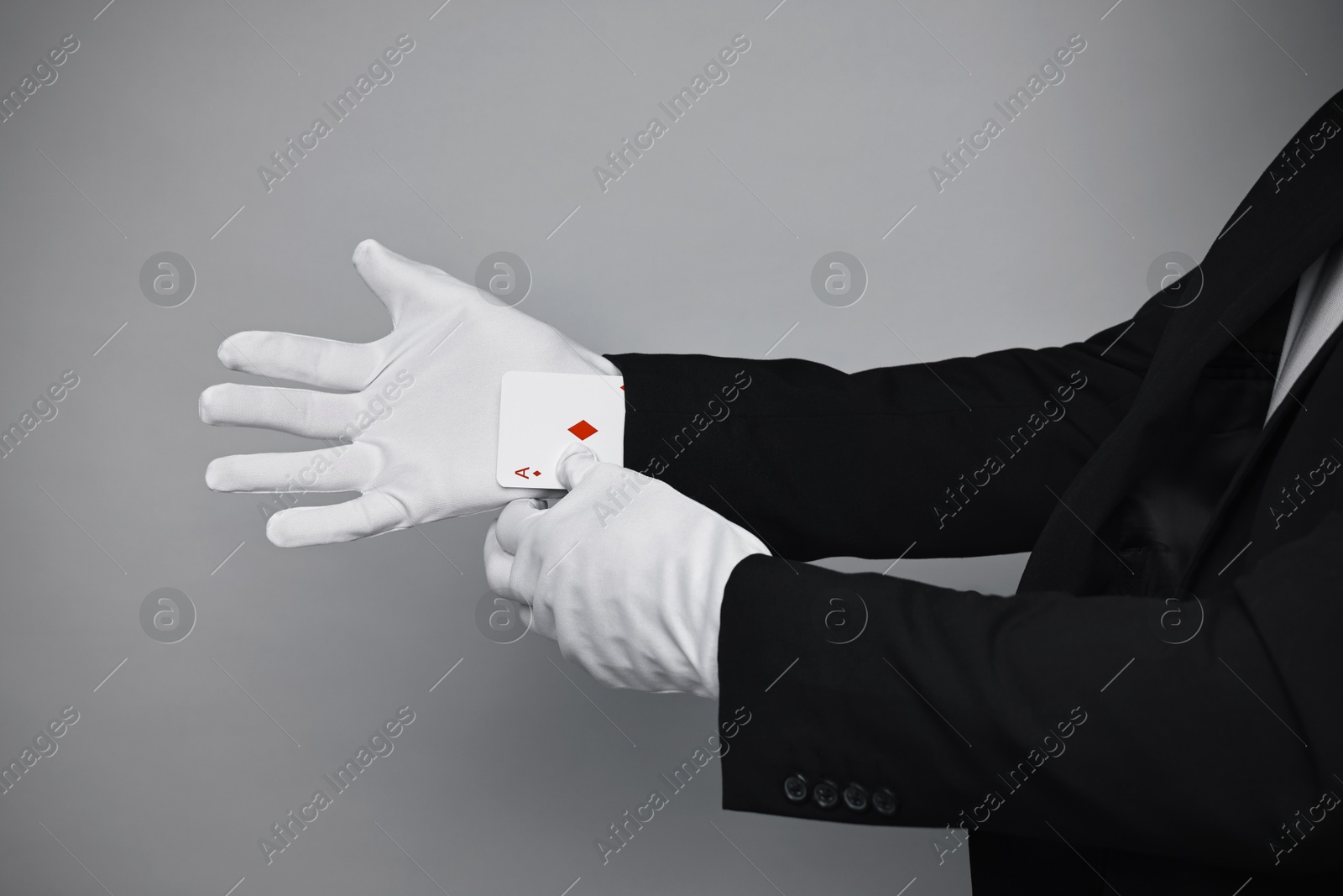 Photo of Illusionist taking playing card out of sleeve on grey background, closeup