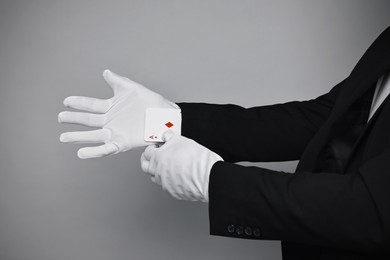 Illusionist taking playing card out of sleeve on grey background, closeup