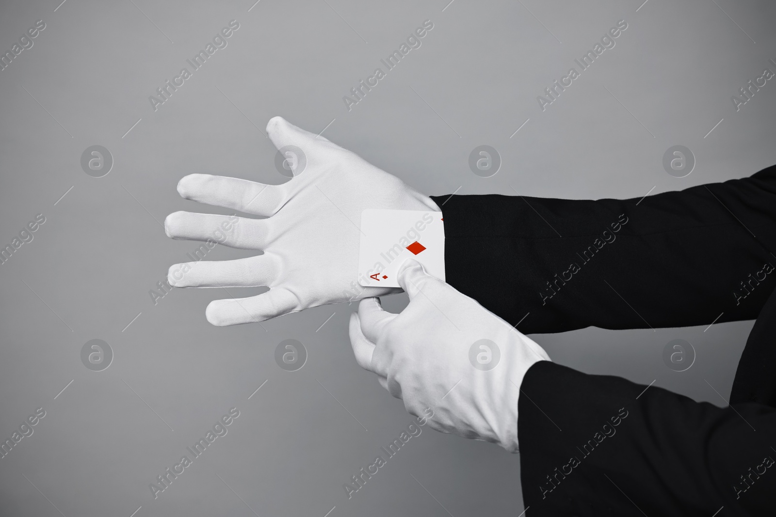 Photo of Illusionist taking playing card out of sleeve on grey background, closeup