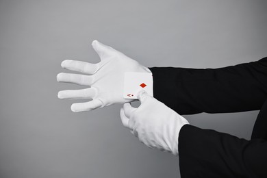 Photo of Illusionist taking playing card out of sleeve on grey background, closeup