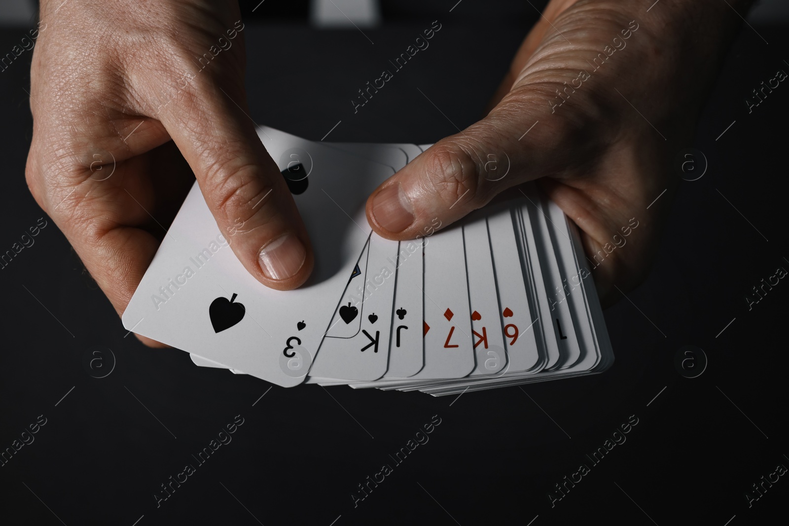 Photo of Illusionist shuffling playing cards on black background, closeup