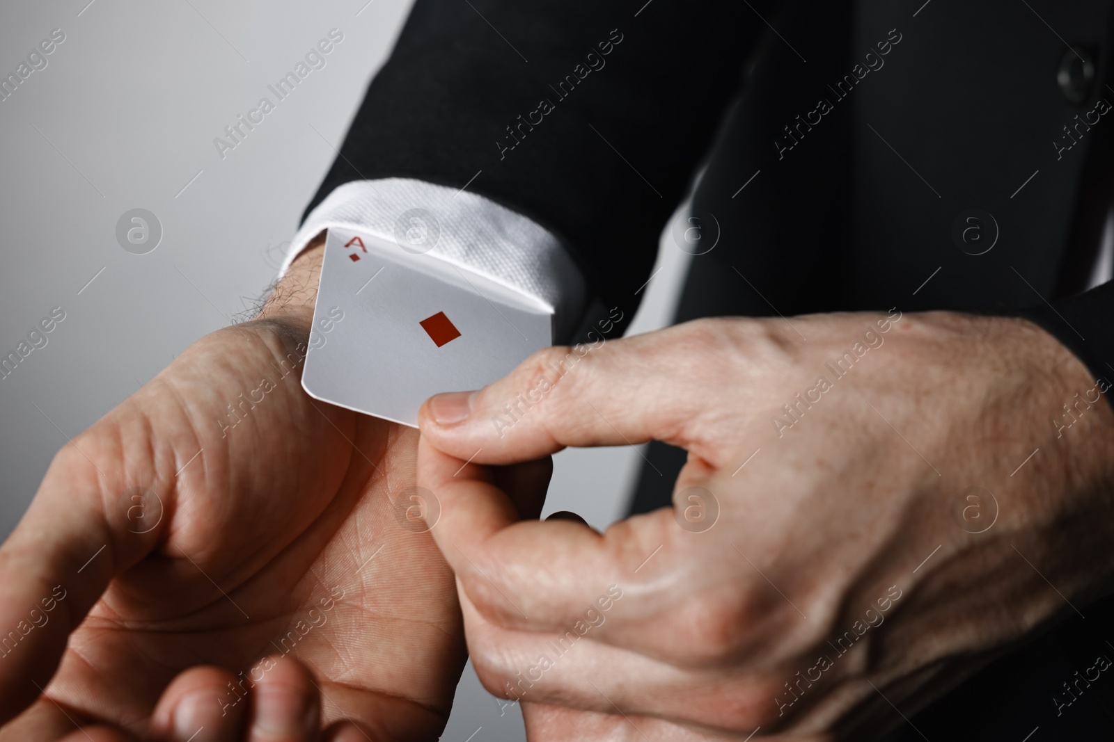 Photo of Illusionist taking playing card out of sleeve on grey background, closeup