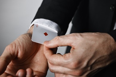 Photo of Illusionist taking playing card out of sleeve on grey background, closeup