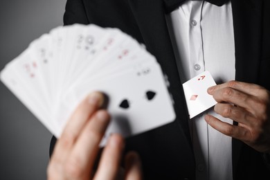 Photo of Illusionist hiding one playing card behind jacket lapel while showing deck on grey background, selective focus