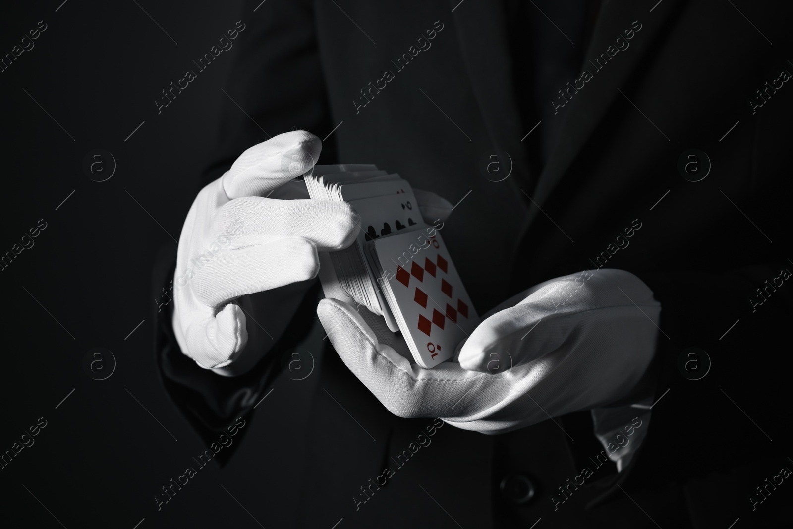 Photo of Illusionist shuffling playing cards on black background, closeup