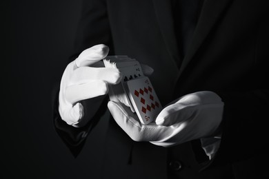 Illusionist shuffling playing cards on black background, closeup