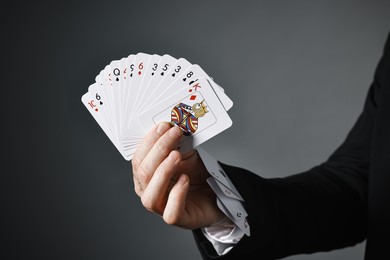 Illusionist with playing cards on grey background, closeup