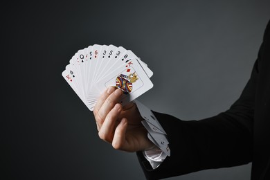 Photo of Illusionist with playing cards on grey background, closeup