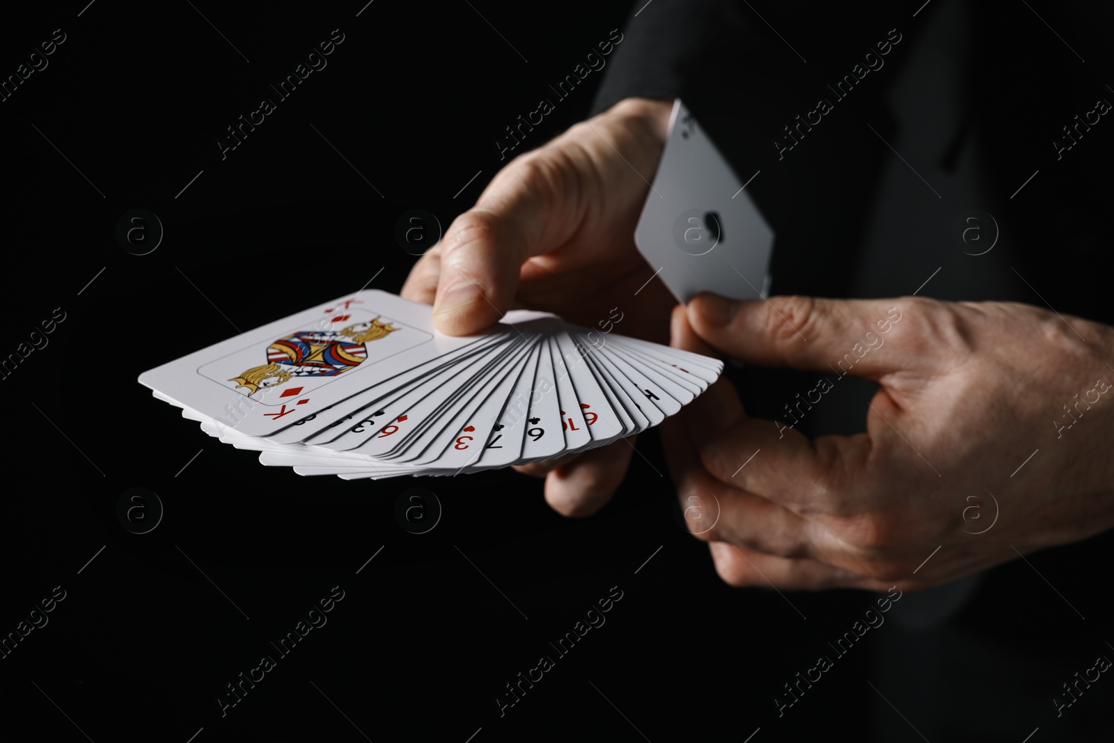 Photo of Illusionist hiding one playing card up his sleeve while showing deck on black background, closeup