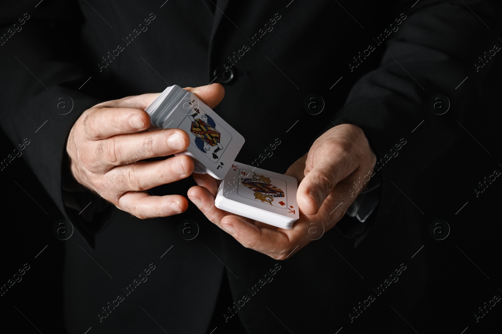 Photo of Illusionist shuffling playing cards on black background, closeup