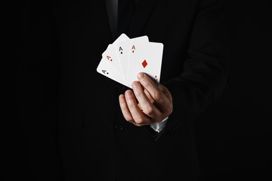 Photo of Illusionist with playing cards on black background, closeup