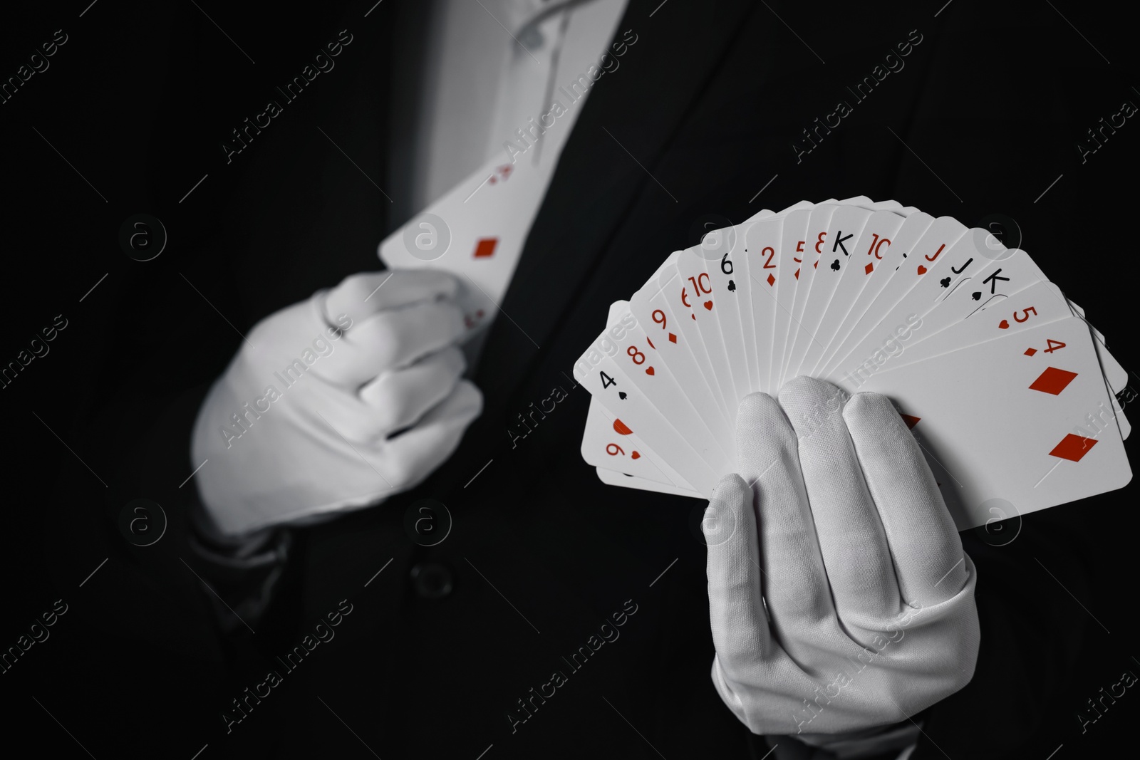 Photo of Illusionist hiding one playing card behind jacket lapel while showing deck on black background, selective focus