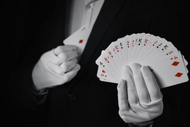 Photo of Illusionist hiding one playing card behind jacket lapel while showing deck on black background, selective focus