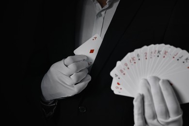 Photo of Illusionist hiding one playing card behind jacket lapel while showing deck on black background, selective focus