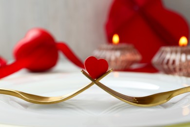 Photo of Romantic table setting for Valentine's day. Decorative heart between forks on white plate, closeup