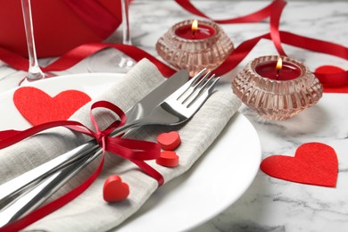 Photo of Romantic place setting for Valentine's day. Plate with cutlery, candles and decorative hearts on white marble table, closeup