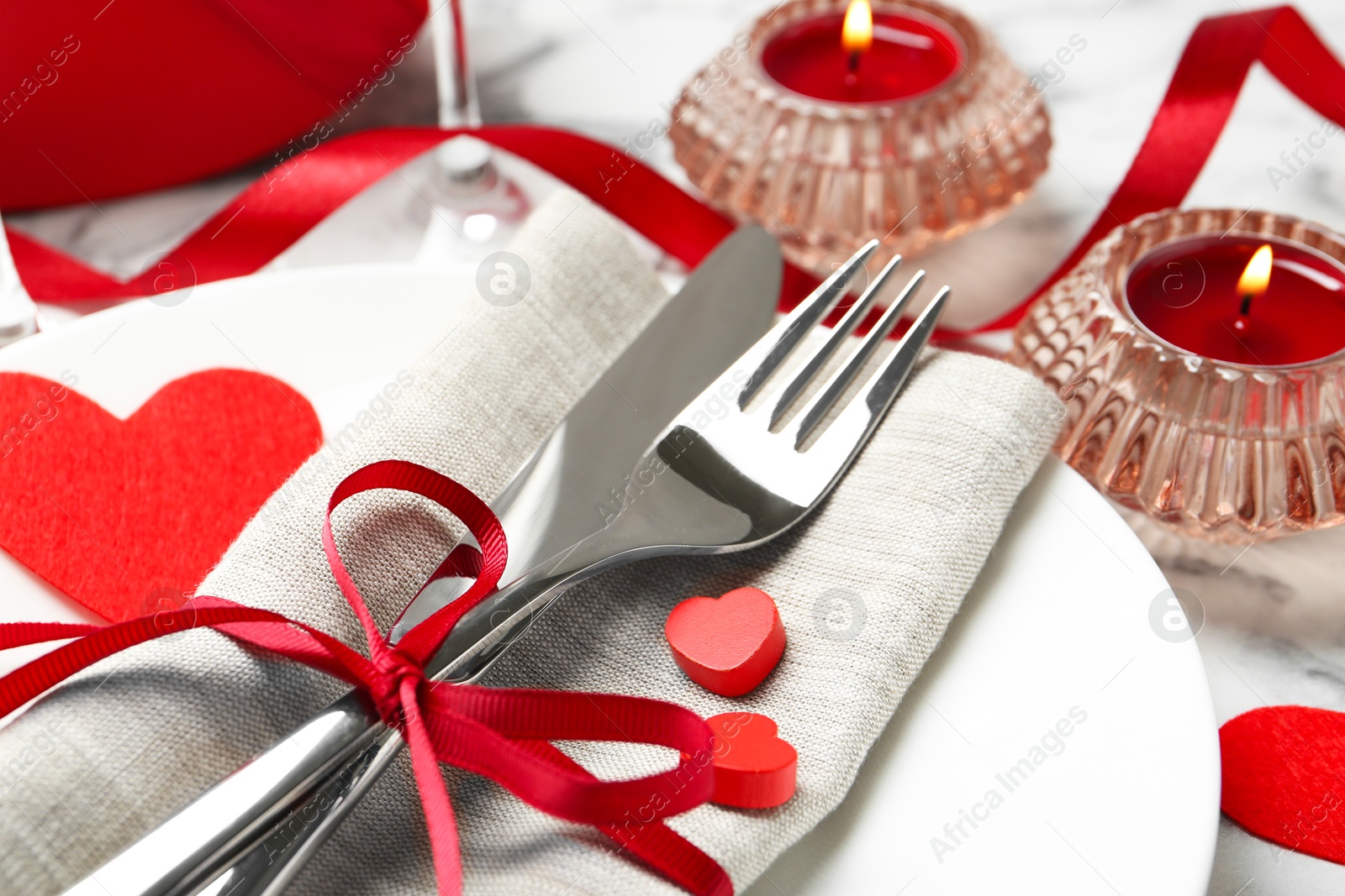 Photo of Romantic place setting for Valentine's day. Plate with cutlery, candles and decorative hearts on white table, closeup