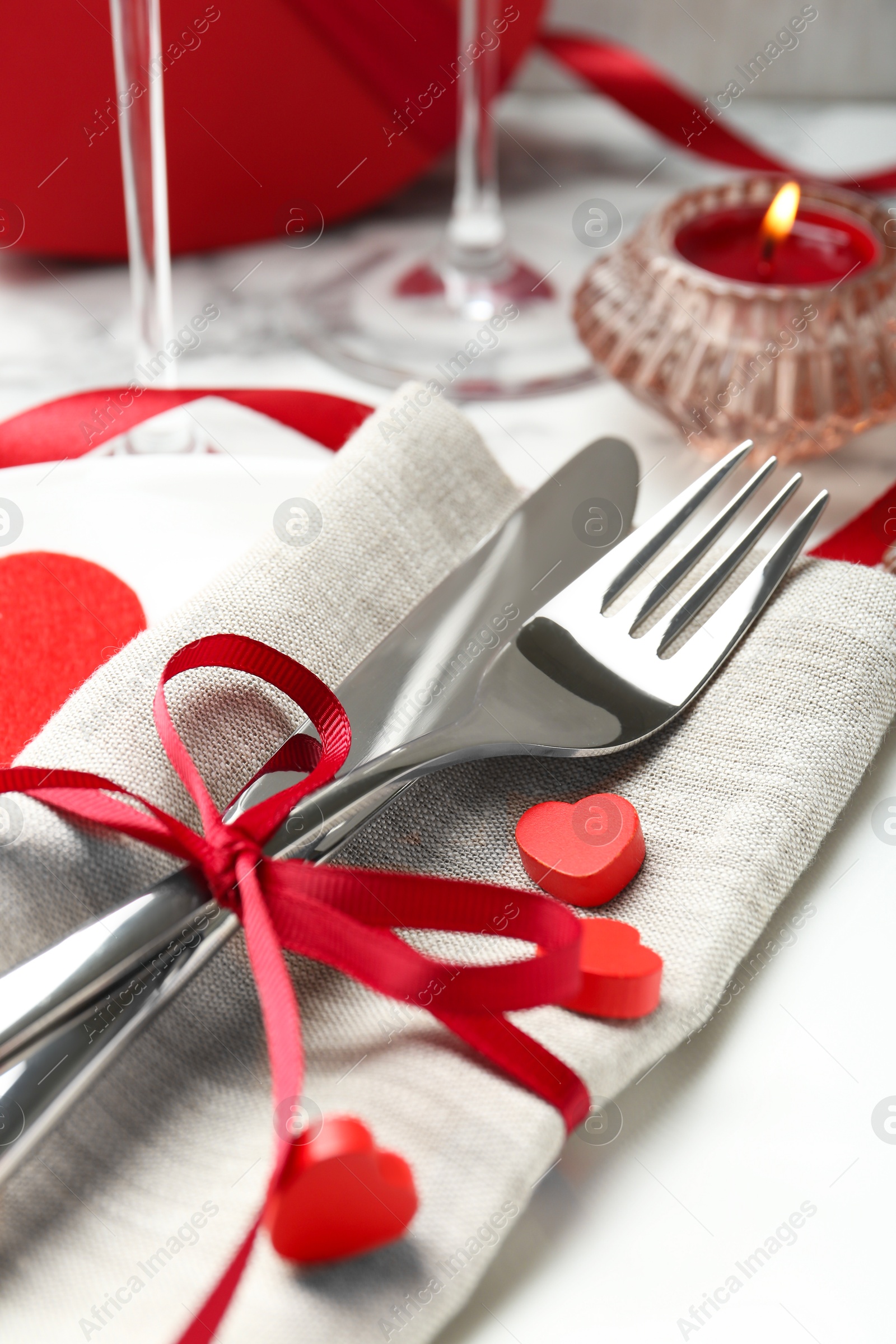 Photo of Romantic place setting for Valentine's day. Plate with cutlery, candle and decorative hearts on white table, closeup