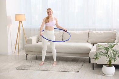 Photo of Beautiful young woman exercising with hula hoop at home