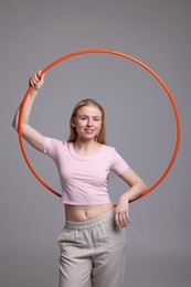 Beautiful young woman with hula hoop on grey background