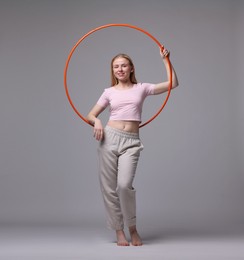 Beautiful young woman with hula hoop on grey background