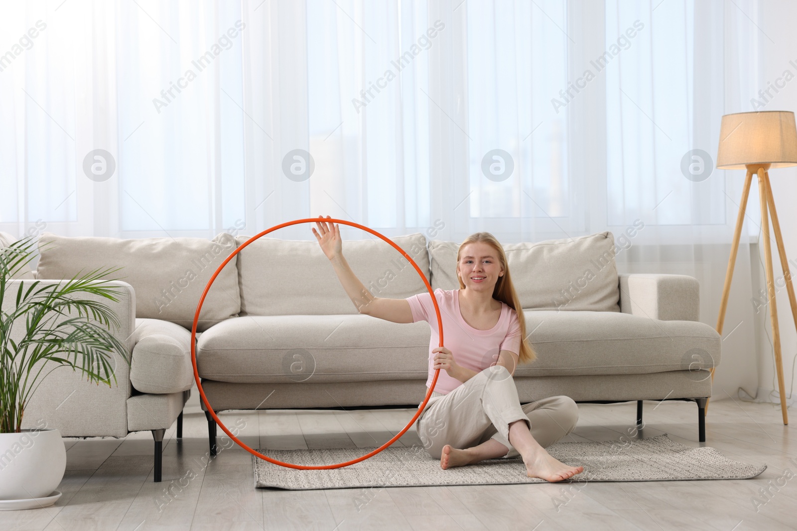 Photo of Beautiful young woman with hula hoop on floor at home