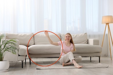 Photo of Beautiful young woman with hula hoop on floor at home