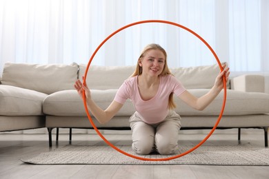 Photo of Beautiful young woman with hula hoop on floor at home