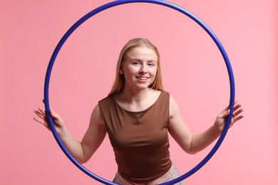 Beautiful young woman with hula hoop on pink background