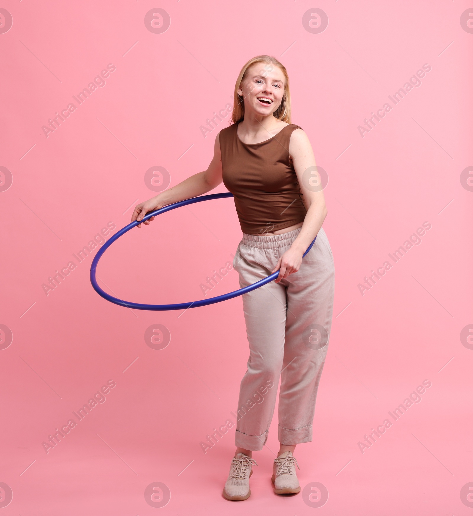 Photo of Beautiful young woman exercising with hula hoop on pink background, space for text