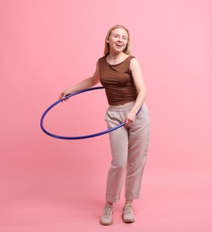 Beautiful young woman exercising with hula hoop on pink background, space for text