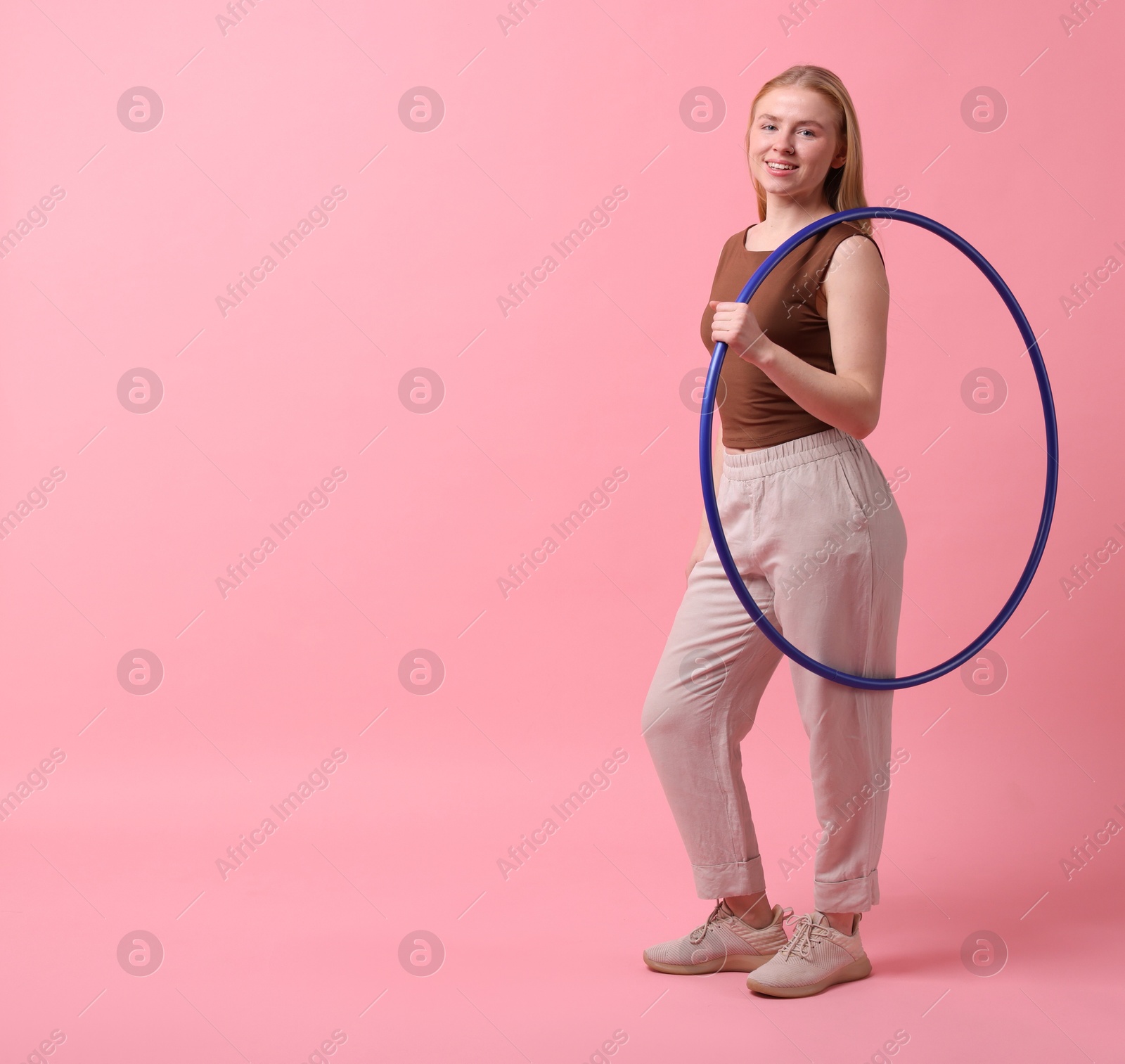 Photo of Beautiful young woman with hula hoop on pink background, space for text