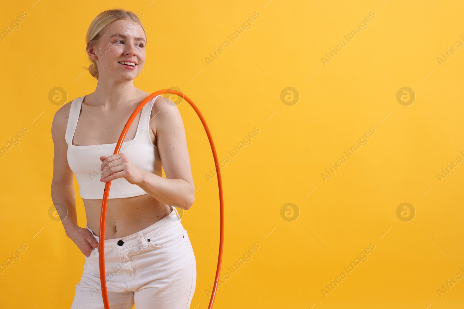 Photo of Beautiful young woman with hula hoop on yellow background, space for text