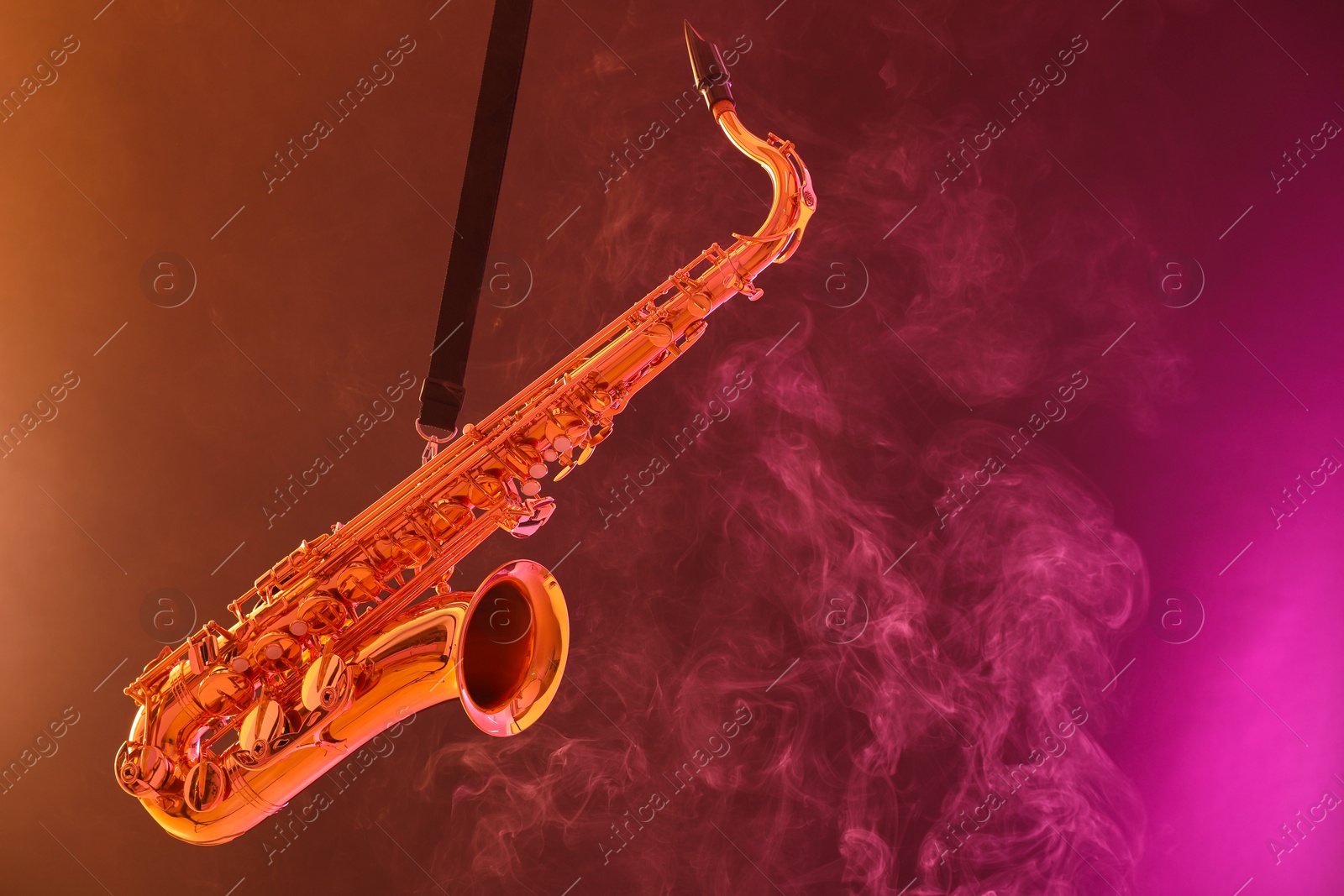 Photo of Golden saxophone on color background with smoke. Space for text