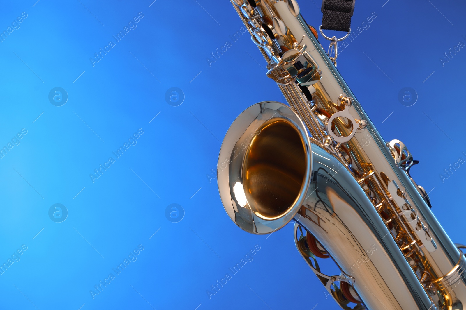 Photo of Golden saxophone on blue background, closeup. Space for text