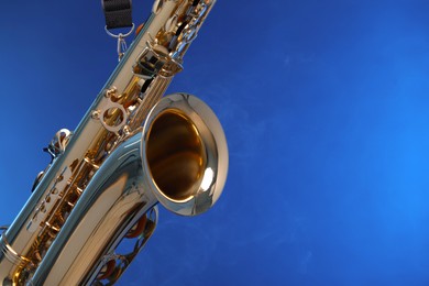 Photo of Golden saxophone on blue background, closeup. Space for text