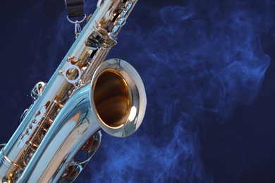 Golden saxophone on dark blue background with smoke, closeup. Space for text