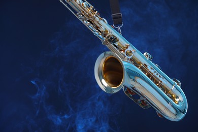 Golden saxophone on dark blue background with smoke, closeup. Space for text