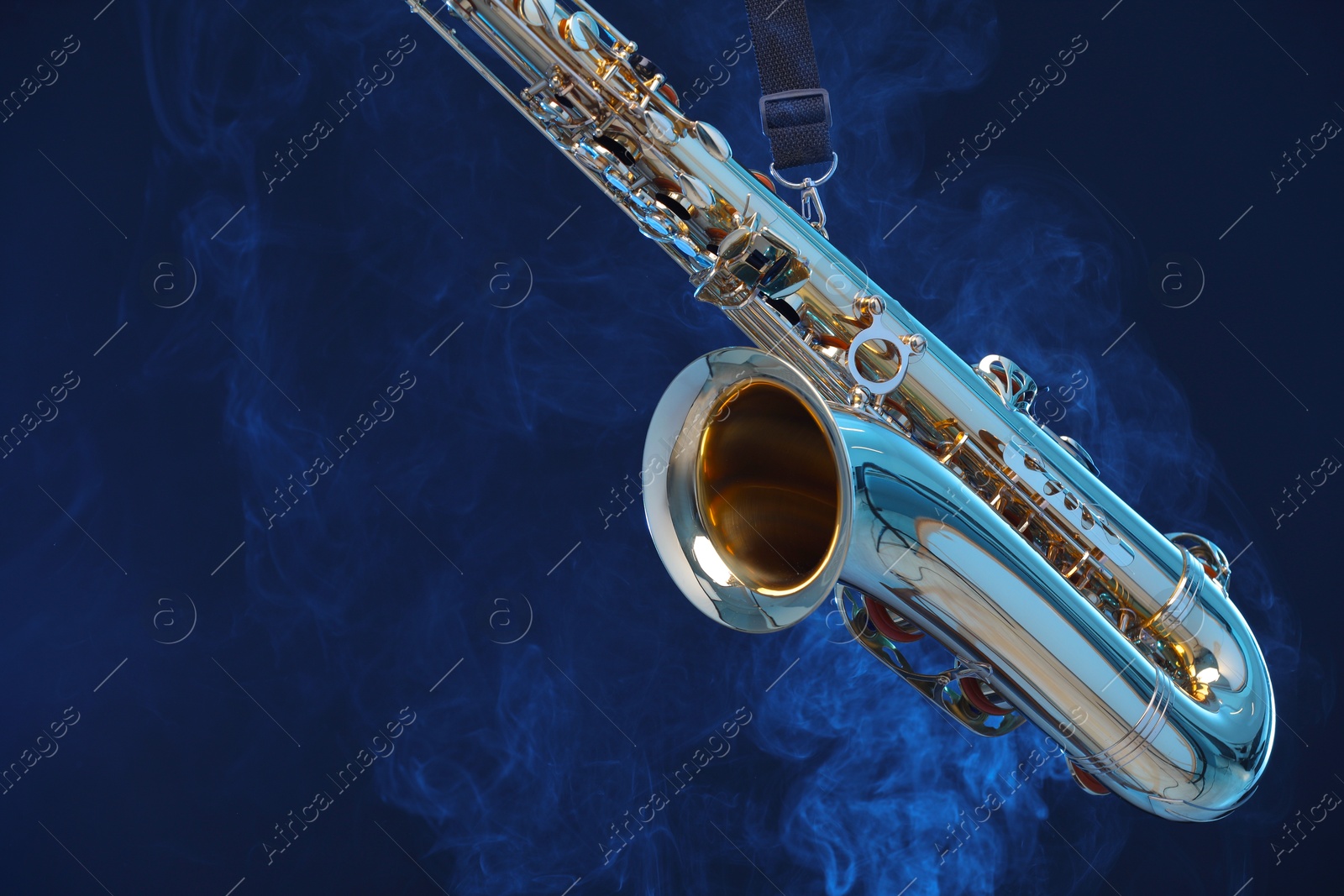 Photo of Golden saxophone on dark blue background with smoke, closeup. Space for text