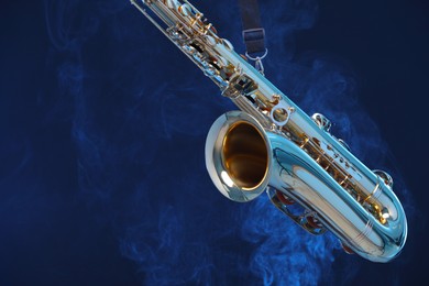 Photo of Golden saxophone on dark blue background with smoke, closeup. Space for text