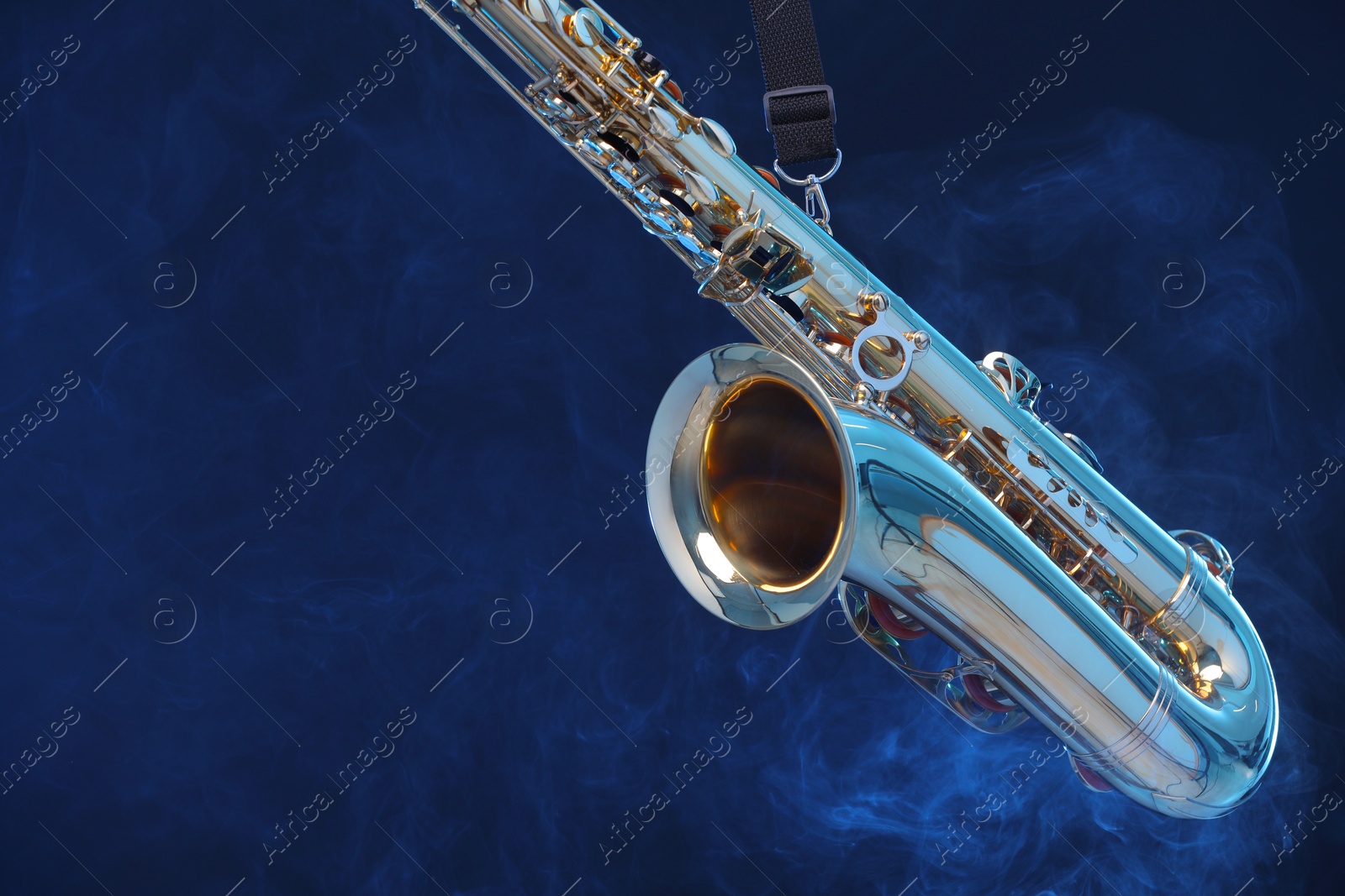 Photo of Golden saxophone on dark blue background with smoke, closeup. Space for text