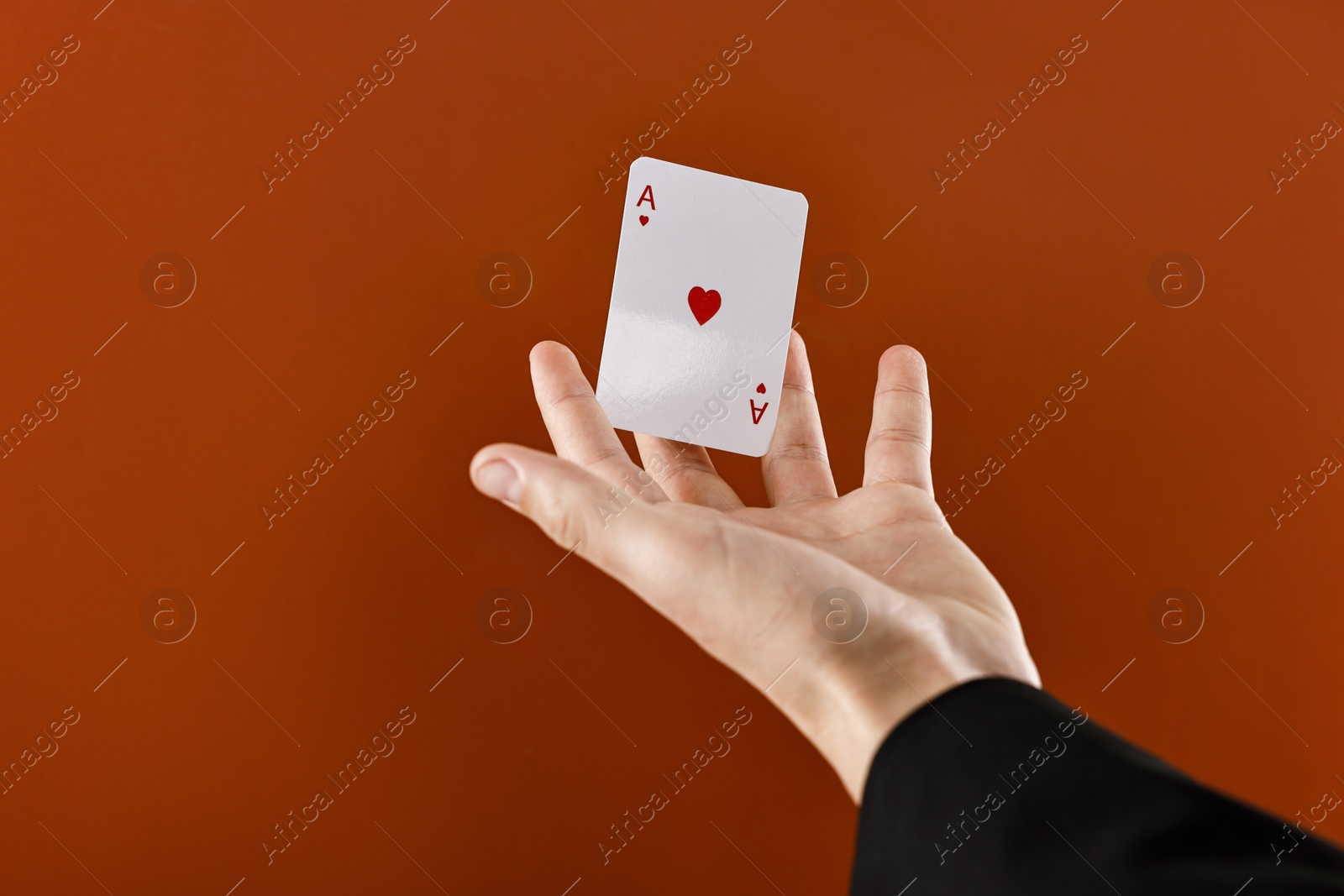 Photo of Illusionist showing playing card on dark orange background, closeup. Space for text