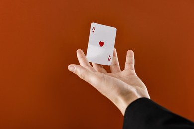 Illusionist showing playing card on dark orange background, closeup. Space for text