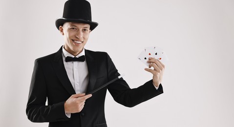 Photo of Illusionist pointing magic wand on playing cards against white background. Space for text