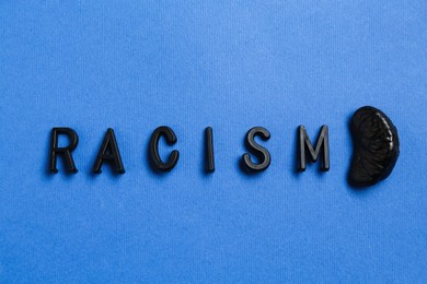 Photo of Word Racism and black tangerine segment on blue background, top view