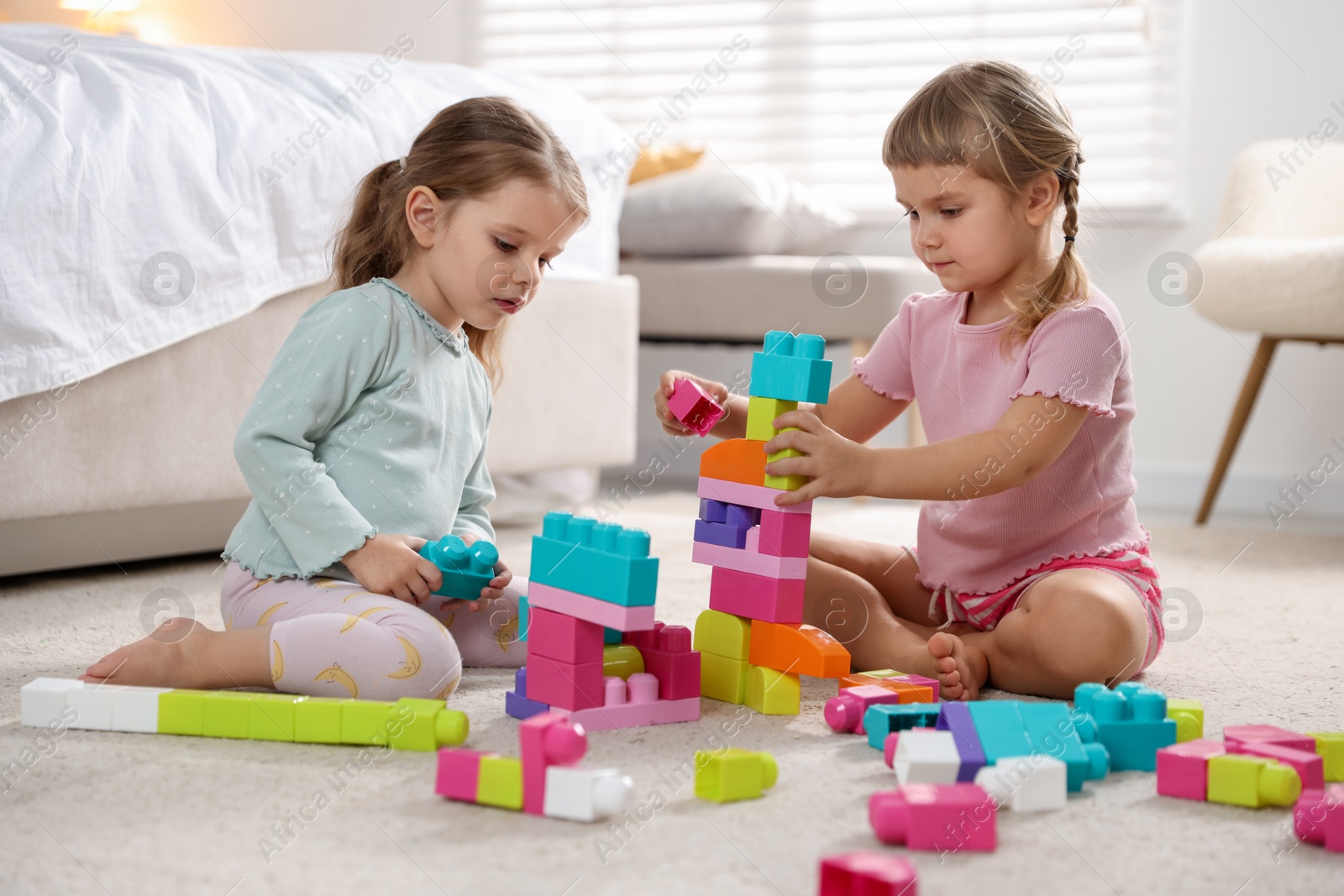 Photo of Cute little sisters playing with colorful building blocks on floor at home