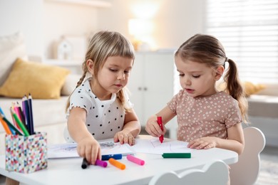 Cute little sisters drawing at white table in room