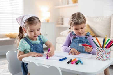 Cute little sisters drawing at white table in room