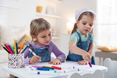 Cute little sisters drawing at white table in room